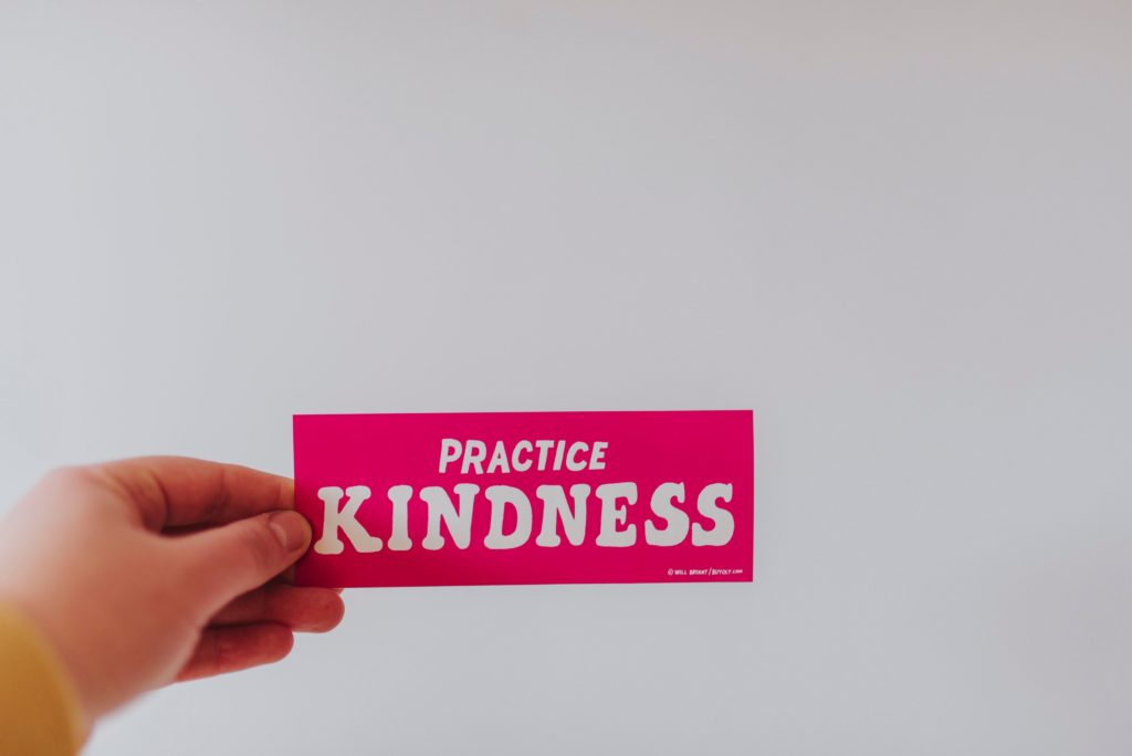 a hand holding a card with the words PRACTICE KINDNESS on